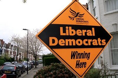 A Lib Dem orange diamond poster in a garden on a terraced street